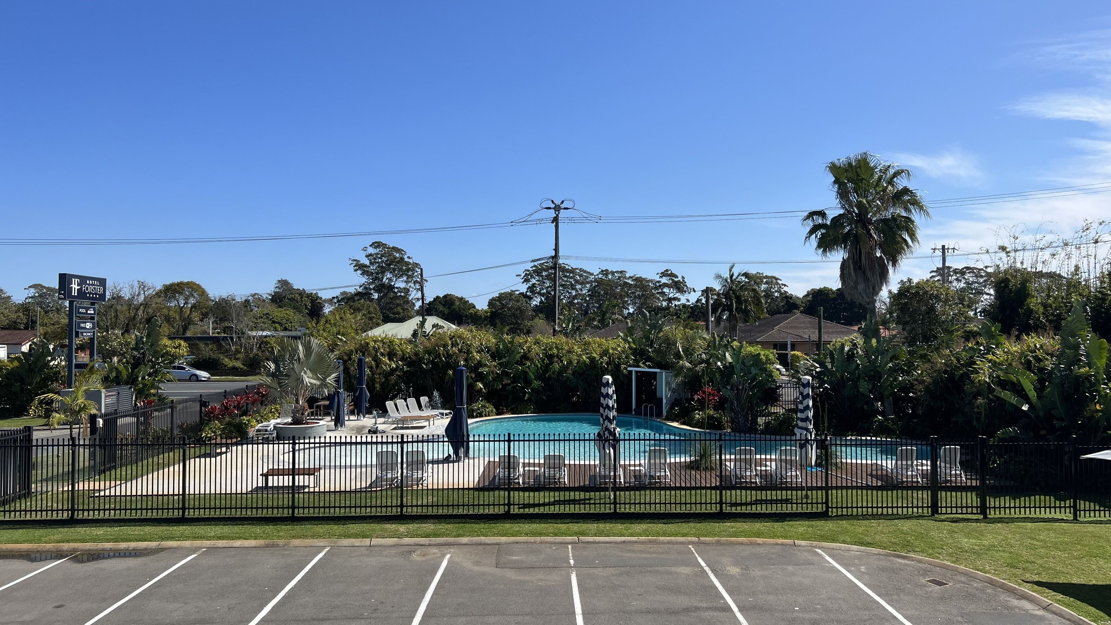 A hotel with a swimming pool, surrounded by a fence and lush greenery.