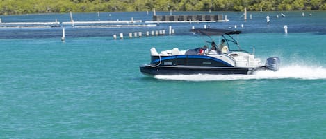 A speedboat on a turquoise body of water with a dock in the background.