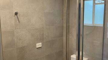 Un baño moderno con cabina de ducha de vidrio, inodoro blanco y lavabo redondo sobre encimera de madera.