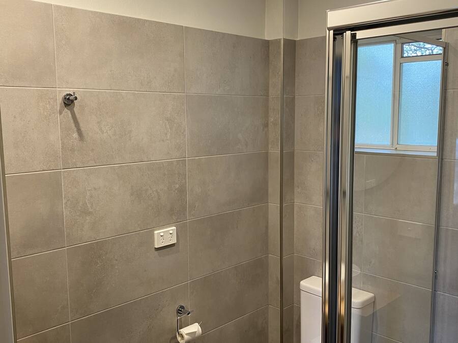Un baño moderno con cabina de ducha de vidrio, inodoro blanco y lavabo redondo sobre encimera de madera.