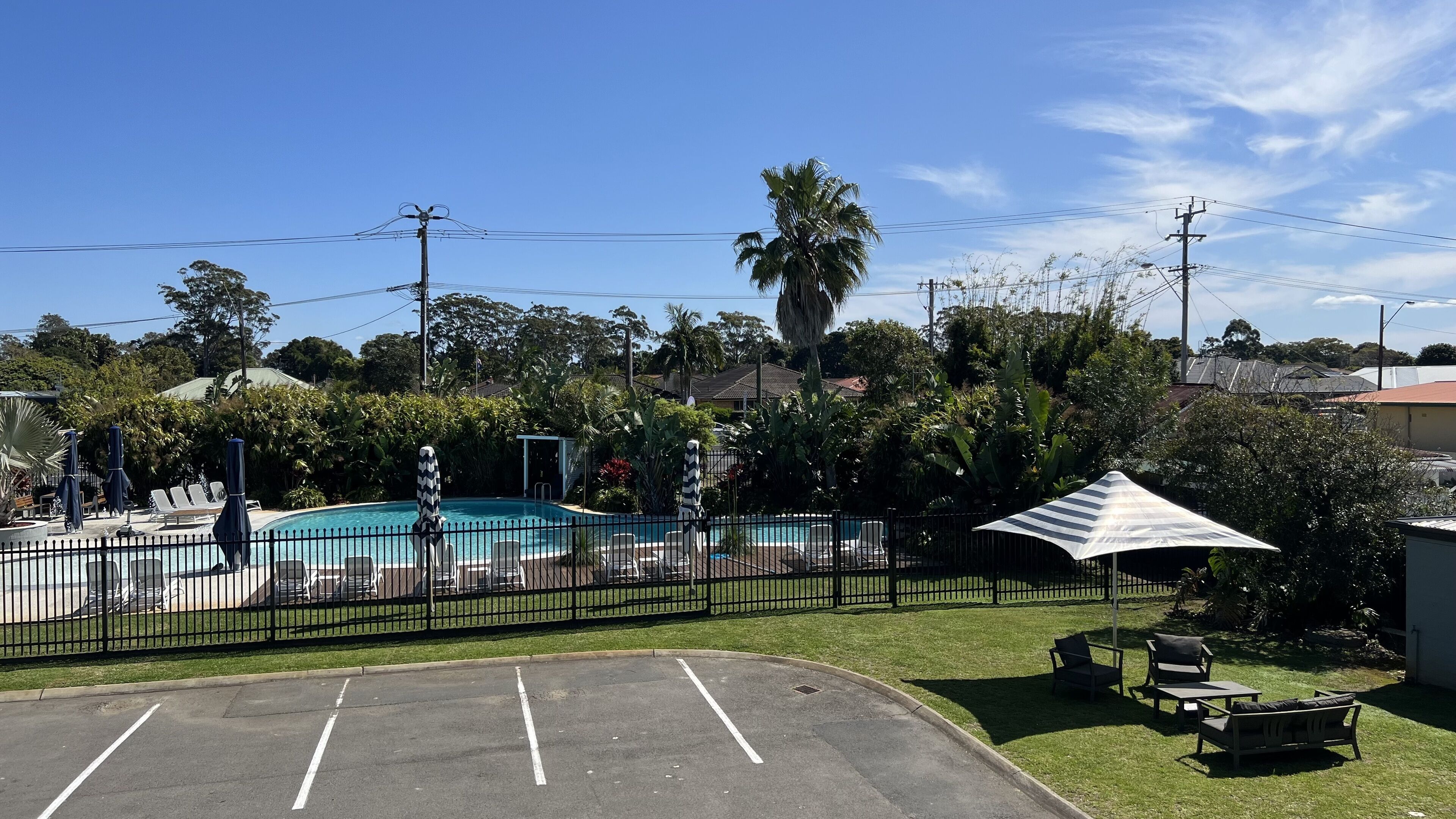 A swimming pool with lounge chairs and umbrellas, surrounded by a fence and greenery.