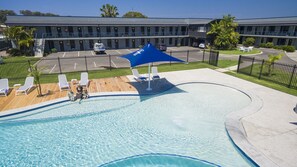 A swimming pool with lounge chairs and a blue umbrella, surrounded by a fenced deck area.