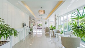 A modern hotel lobby with a long reception desk, seating area, and large windows offering views of the outdoors. - Park 38 Hotel (Wichit)