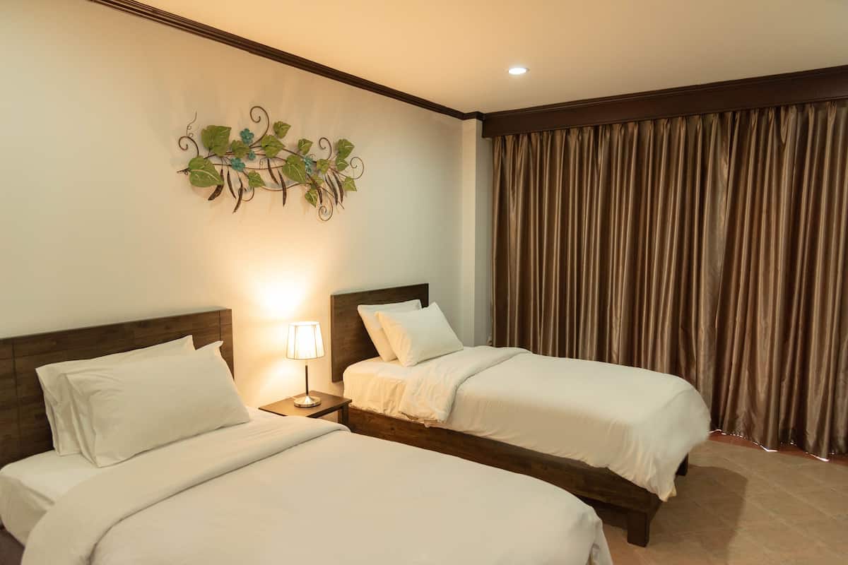 Une chambre d’hôtel avec deux lits, une table de chevet avec une lampe, un élément décoratif mural et une grande fenêtre avec des rideaux.