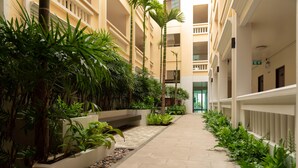 A corridor with a tiled floor, surrounded by planters with various plants and a palm tree. - Park 38 Hotel (Wichit)