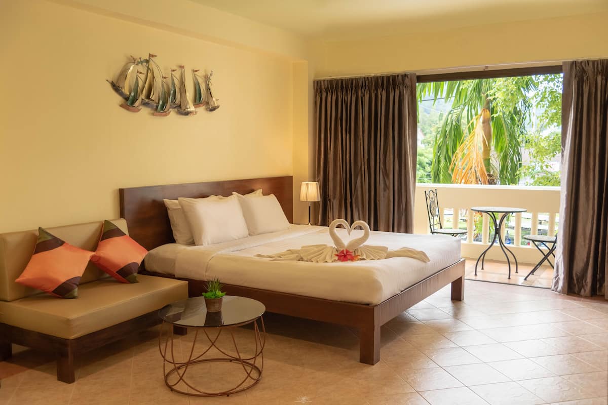 Une chambre d’hôtel comprenant un lit, un canapé, une petite table avec une plante et un balcon avec une table et des chaises.