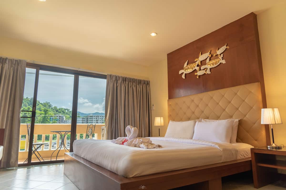 Une chambre d’hôtel avec un grand lit, une tête de lit ornée d’un motif décoratif, une table de chevet avec une lampe et une vue sur l’extérieur grâce à une porte coulissante.