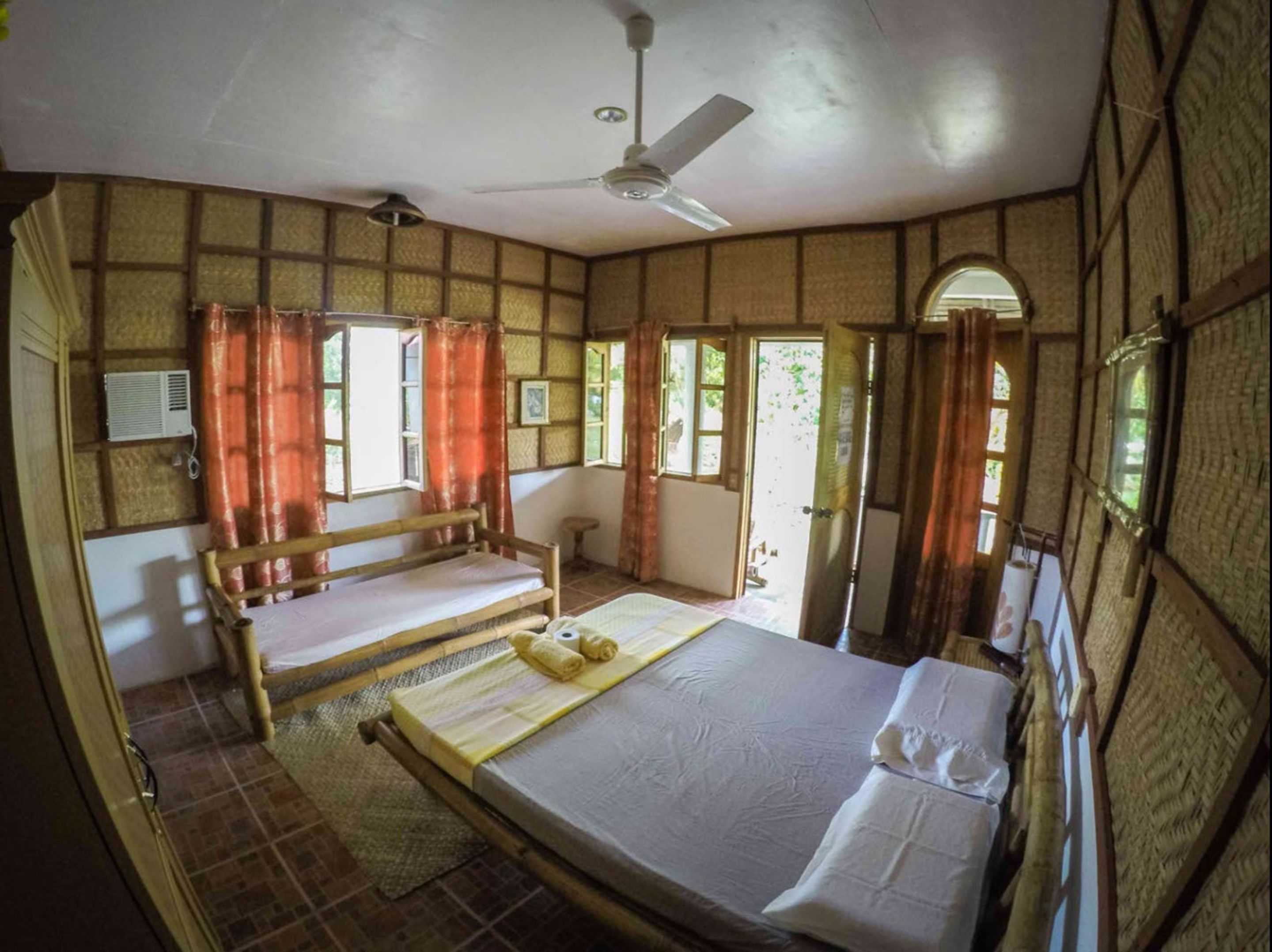 Una habitación con cama, ventilador de techo y ventana con cortinas.