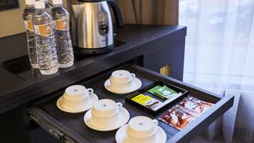 A tray with teapots, teacups, bottled water, and tea packets in a hotel room.