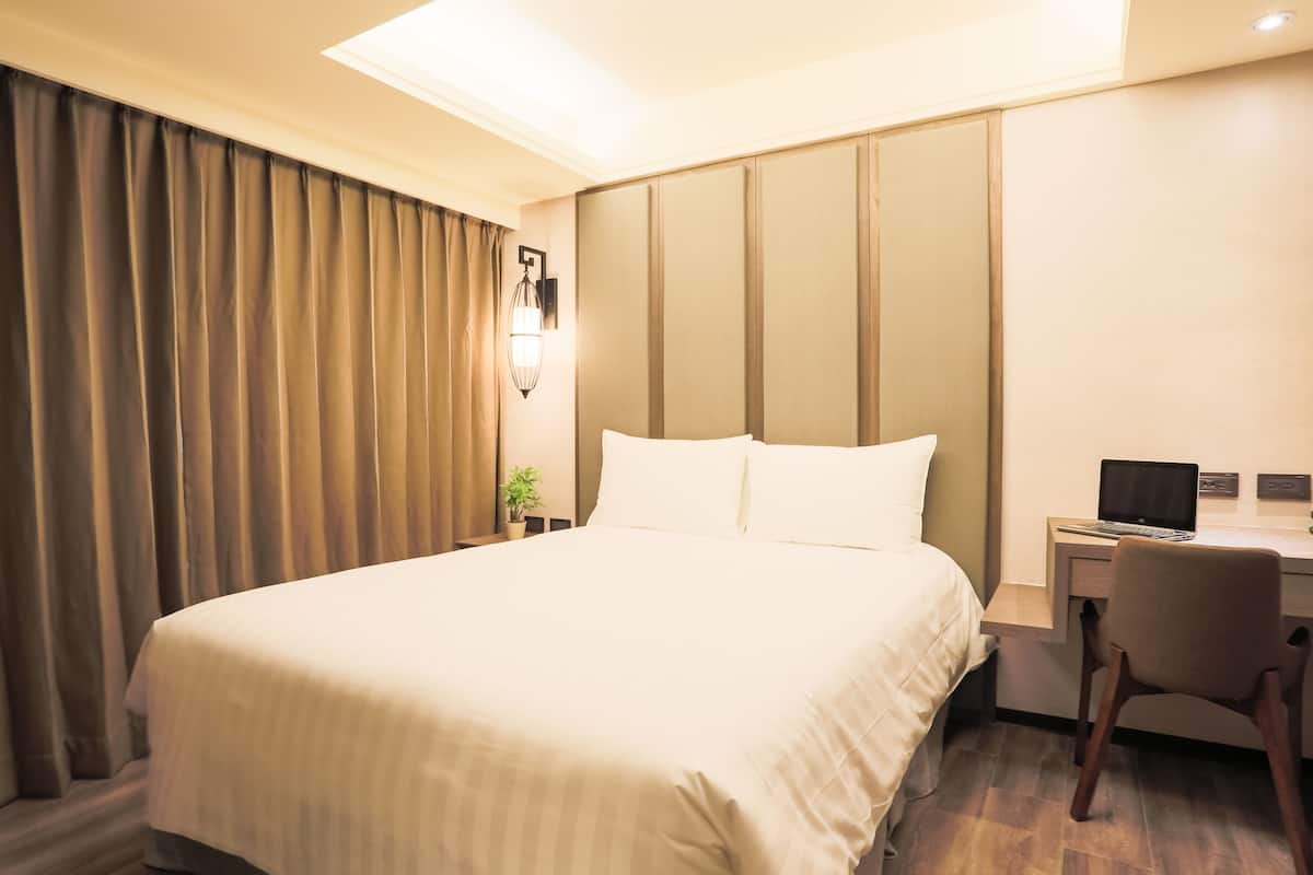 A hotel room with a large bed, a desk with a chair, and a lamp.