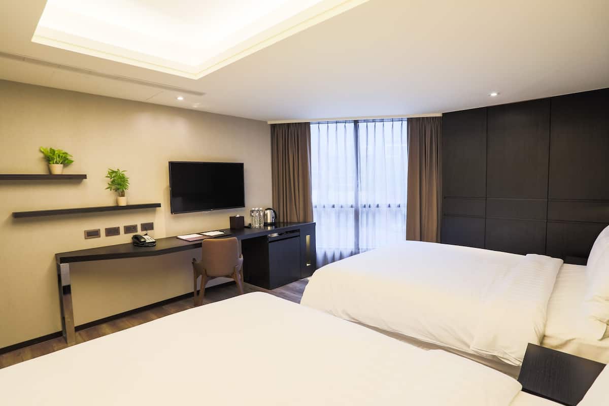 A hotel room with a bed, a desk, a chair, a television, and a window with curtains.