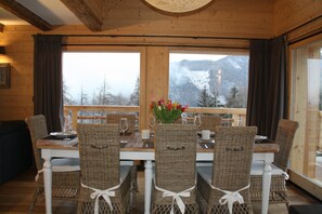 A dining area with a table set for four, wicker chairs with white cushions, and a vase of flowers.