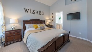 Ein Schlafzimmer mit einem Bett, Nachttischen, einem Fernseher und einer Wand mit dem Schriftzug 'WISHES'.