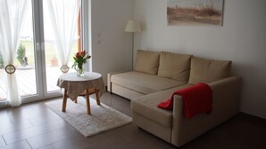 Una sala de estar con un sofá color beige, una mesita redonda con un jarrón de flores, una lámpara y un cuadro en la pared.