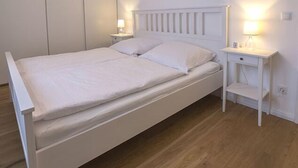 Una cama blanca con dos almohadas y una mesita de noche con una lámpara.