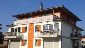 Una casa moderna de dos pisos con techo plano, ventanas amplias y un balcón.