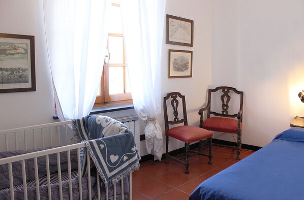 A room with a crib, a chair, a bed, and a window with curtains.