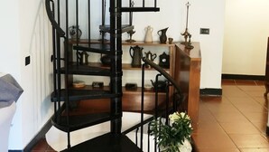 Eine Wendeltreppe mit schwarzer Handläufe, die zu einer Zwischenebene führt, auf der Regale verschiedene Gegenstände tragen.