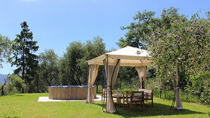 Ein überdachter Außenbereich mit Tisch und Stühlen, einer hölzernen Bank und einem Whirlpool.