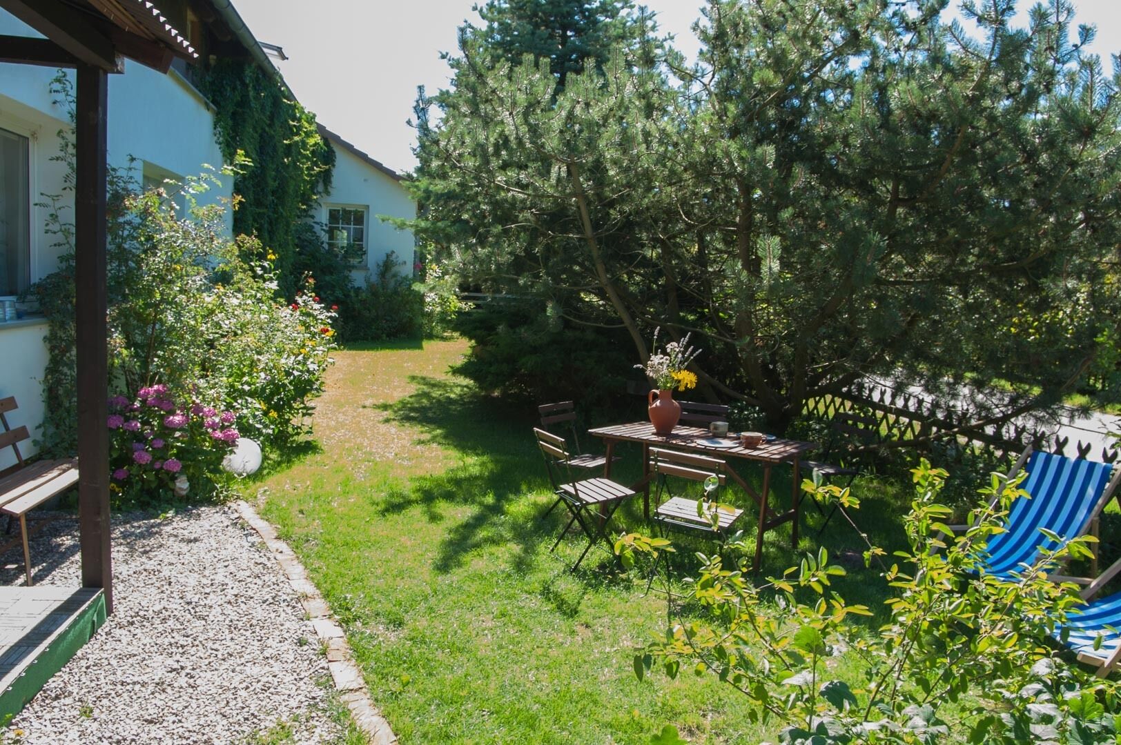A garden with a wooden table and chairs, a bench, and a blue striped chair.