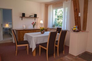 A dining area with a table set for four, chairs, a vase with flowers, a lamp, and speakers on a shelf. - Beautiful, spacious apartment at the gates of the Hanseatic city of Rostock  (Lambrechtshagen)