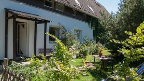 A house with a covered porch, a lawn, and a garden with various plants and a bench. - Beautiful, spacious apartment at the gates of the Hanseatic city of Rostock  (Lambrechtshagen)