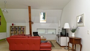 A spacious living room with a red sofa, a wooden coffee table, a bookshelf, a TV, and a small side table with a vase. - Beautiful, spacious apartment at the gates of the Hanseatic city of Rostock  (Lambrechtshagen)