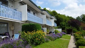 A two-story building with balconies, a gravel pathway, and a variety of flowers. - Vacation apartment Sielbeck, vacation with dog, WLAN available  (Eutin)
