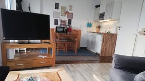 A living room with a TV, wooden furniture, a kitchen area with cabinets and appliances, and a grey sofa. - Vacation apartment Sielbeck, vacation with dog, WLAN available  (Eutin)