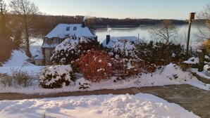 A house with a snow-covered roof, a chimney, and a view of a lake. - Vacation apartment Sielbeck, vacation with dog, WLAN available  (Eutin)