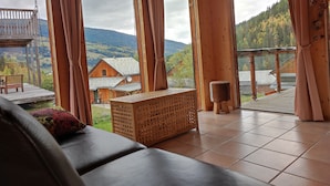 Una baita di legno con un'ampia finestra, una panca imbottita e vista su un paesaggio montano.