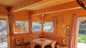 Un interno in legno con un tavolo da pranzo e sedie, ampie finestre con tende e vista su case.