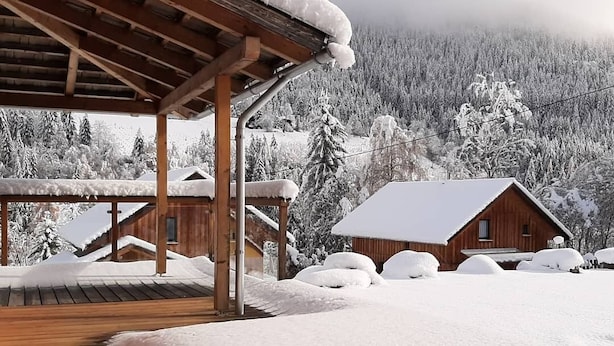 Una baita di legno con tetto innevato e veranda in legno che si protende dall'edificio.