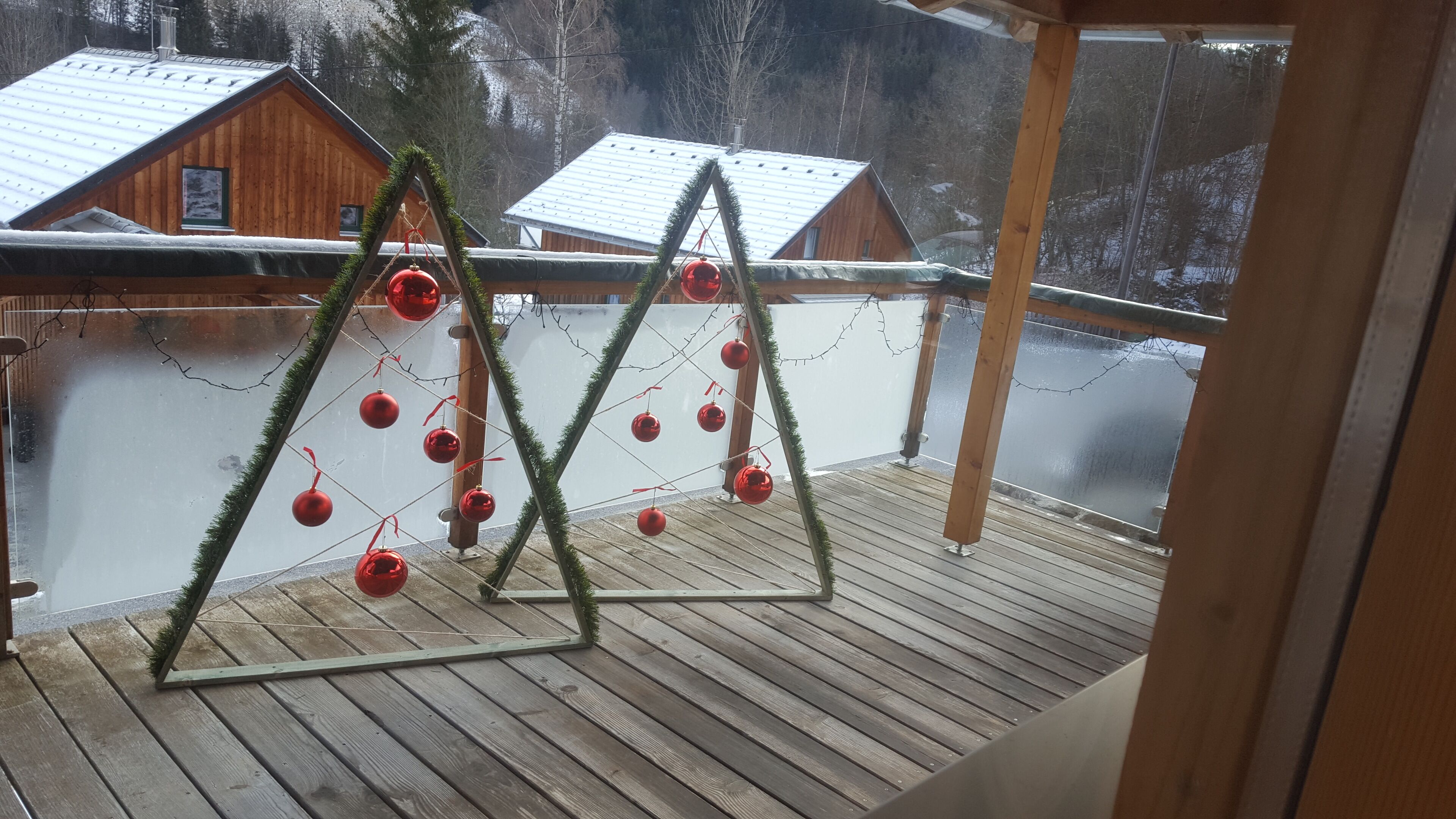 Ett trädäck med ett metallräcke, dekorerat med röda julgransprydnader och gröna växter.