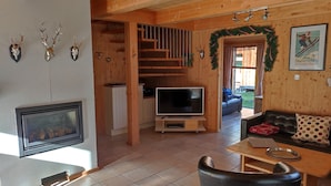 Un interno accogliente di una baita con camino, pareti in legno, una TV, un divano e un'area pranzo.