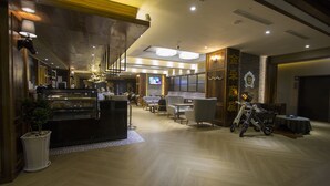 Un hall d’hôtel moderne comprenant un comptoir d’accueil, un espace salon et une exposition de motos.