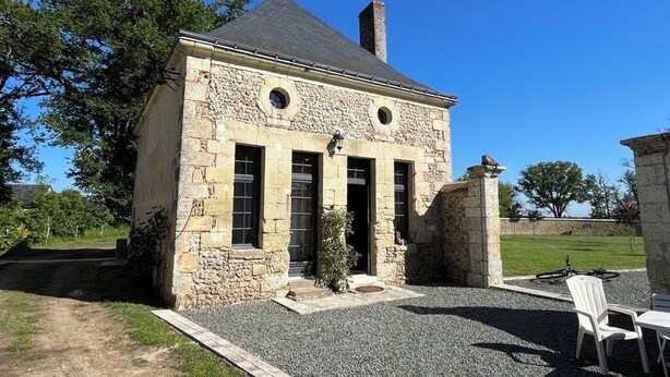 Un edificio in pietra con tetto spiovente, un camino e vialetto sterrato.