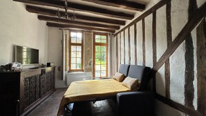 Una stanza con travi a vista in legno, un letto con copriletto giallo, una televisione su un mobile in legno e una finestra con vista sul verde.