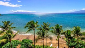 Une plage bordée d’une eau turquoise et limpide, de palmiers et d’une montagne qui se dessine à l’horizon.