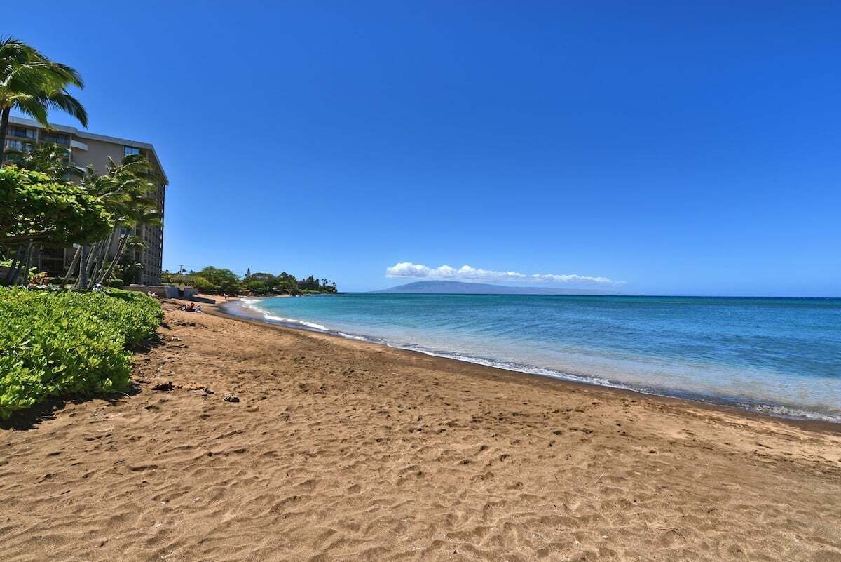 A beach with clear blue water, a sandy shore, and a building with balconies.