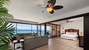 Une chambre spacieuse avec un grand lit, un canapé, un ventilateur de plafond et une vue sur l’océan.