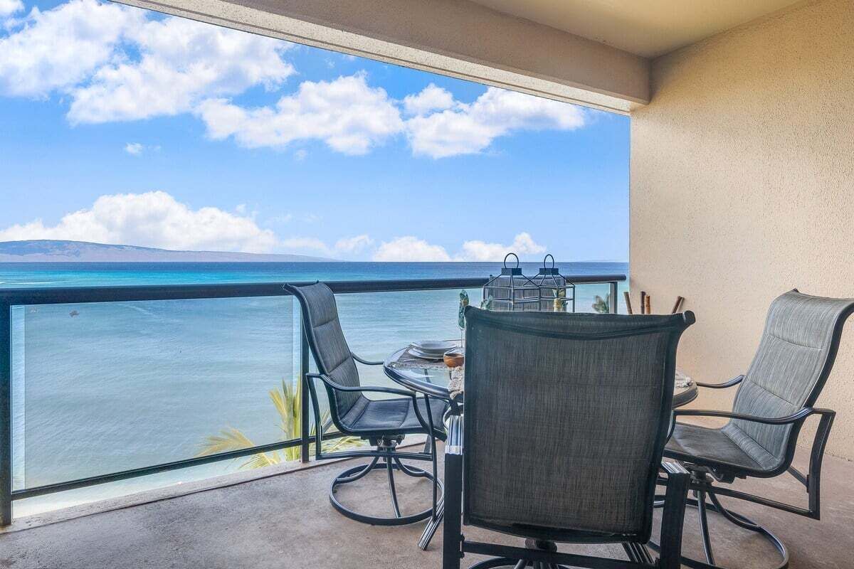 A balcony with a table and chairs, overlooking a body of water and a distant shoreline.