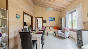 Ett modernt vardagsrum med en matplats, synliga träbjälkar i taket, ett stort fönster med gardiner och en öppen spis.