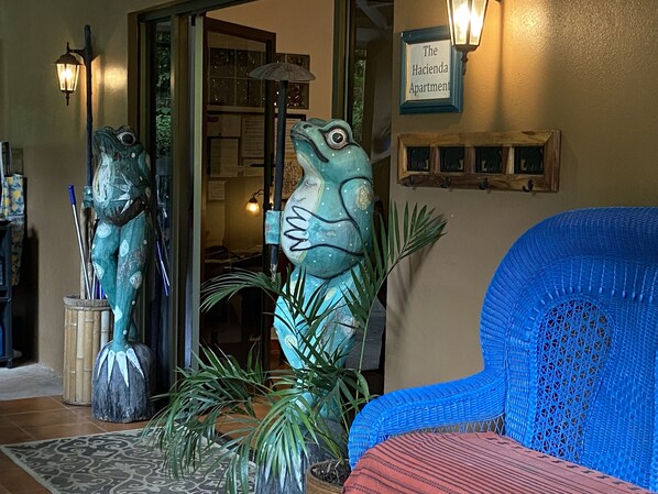 A room with a blue chair, a frog sculpture, and a sign reading "The Hacienda Apartment".