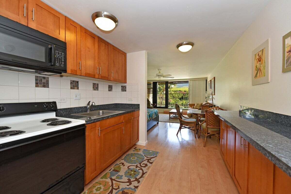 A kitchen with wooden cabinets, a black microwave, and a white stove. There is a dining area with a table and chairs.