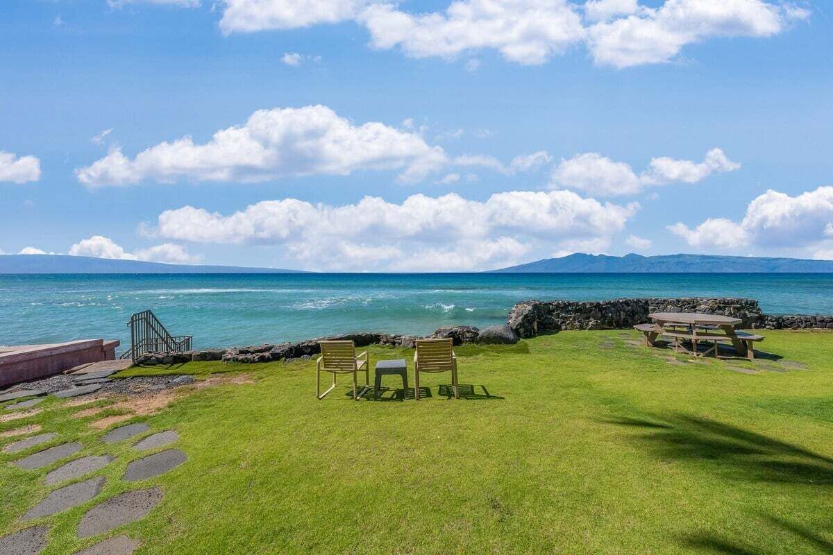 A grassy area with a picnic table and chairs by the ocean, a stone staircase, and a rocky wall.