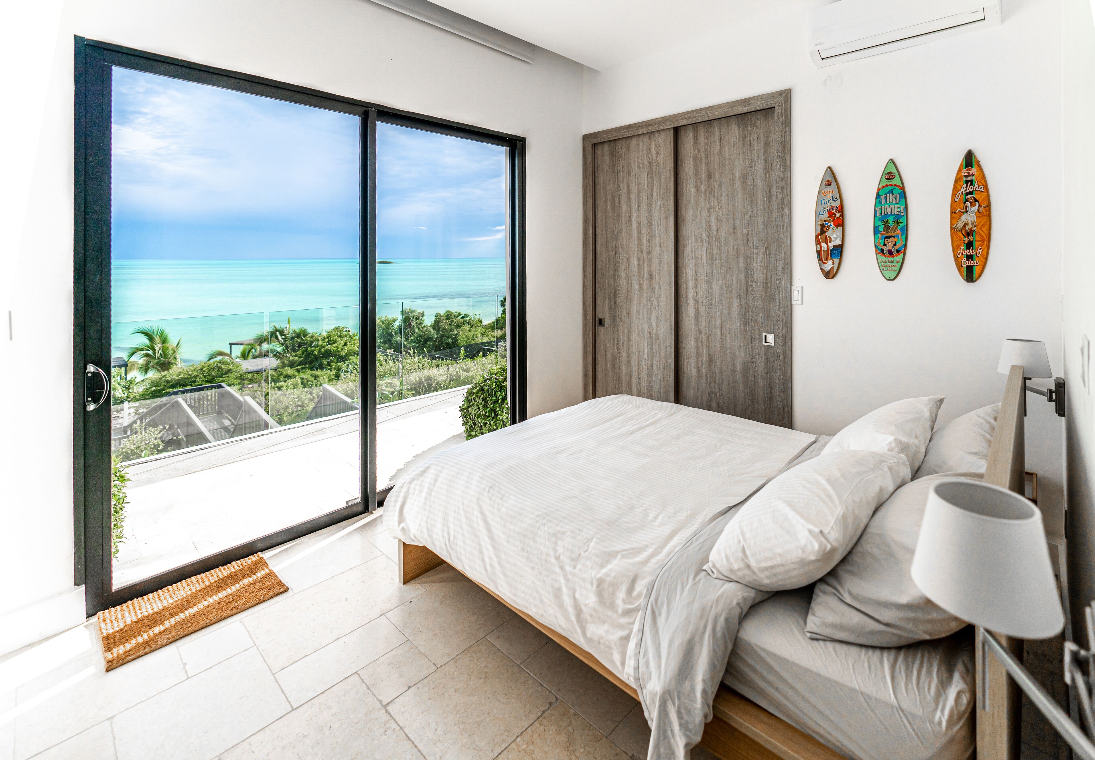 A bedroom with a large sliding glass door leading to a balcony with a view of the ocean.