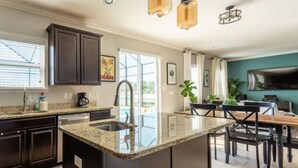 Cocina moderna con muebles oscuros, encimera de granito y una isla central. Hay un comedor con mesa y sillas de madera.