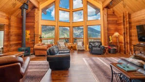 A log cabin interior with a large central window, wooden walls, leather furniture, and a fireplace. - Red Roof Lodge - Leavenworth (Leavenworth)