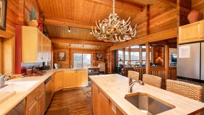 A spacious log cabin kitchen with wooden cabinets, a large island with a sink, and a chandelier. - Red Roof Lodge - Leavenworth (Leavenworth)